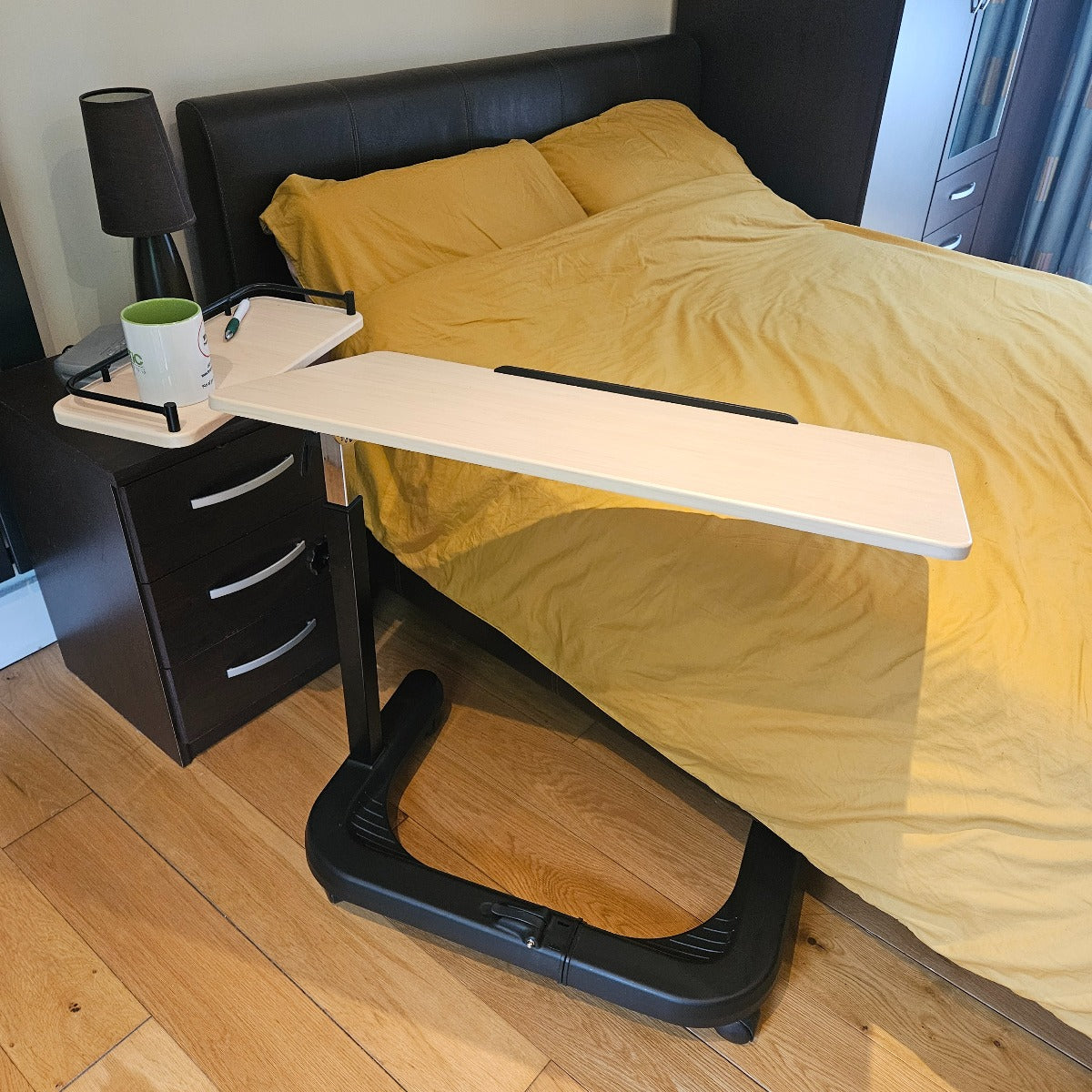 Portable desk attached to a bed with a nightstand and lamp in a bedroom setting.