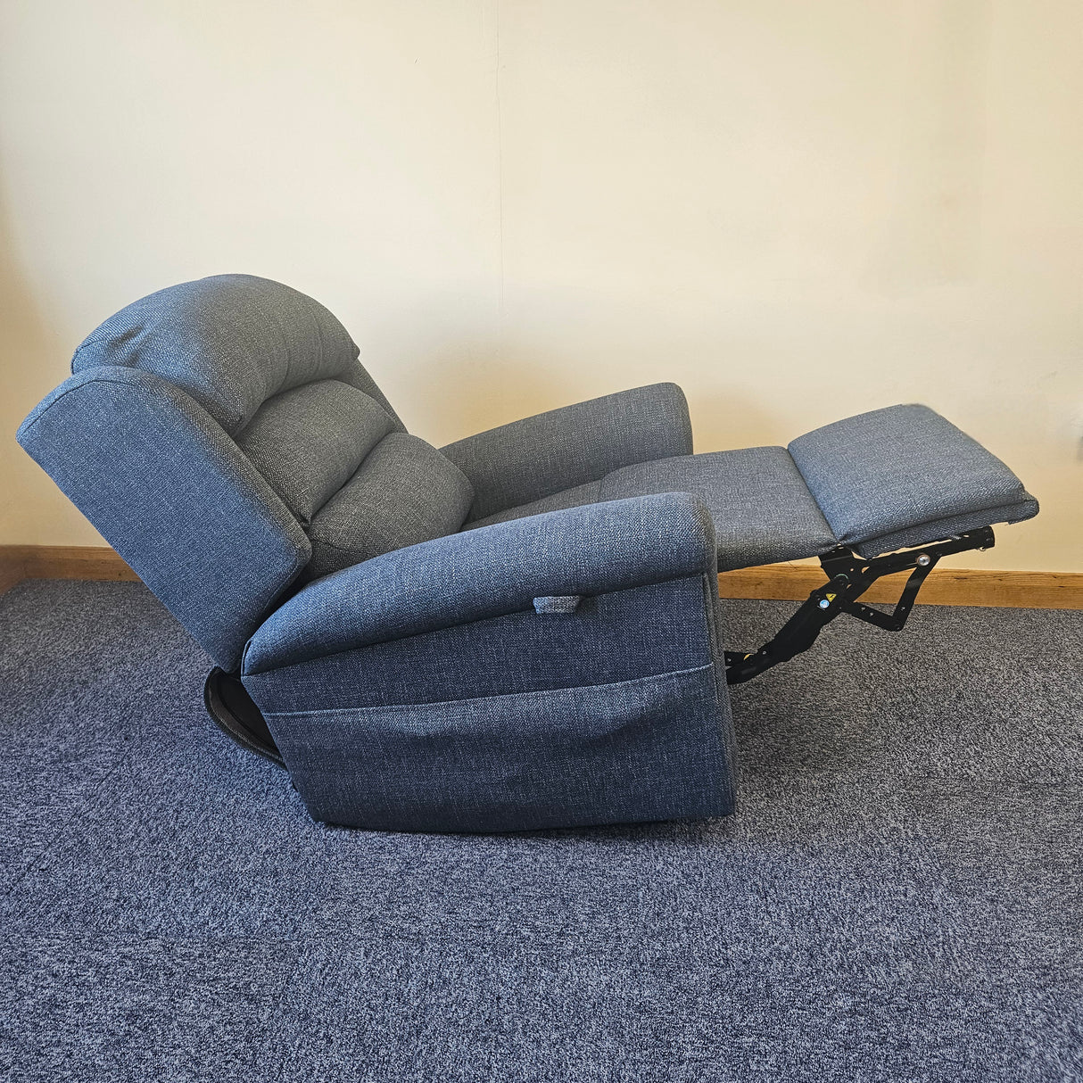 Blue recliner chair with armrests and footrest on a carpeted floor.