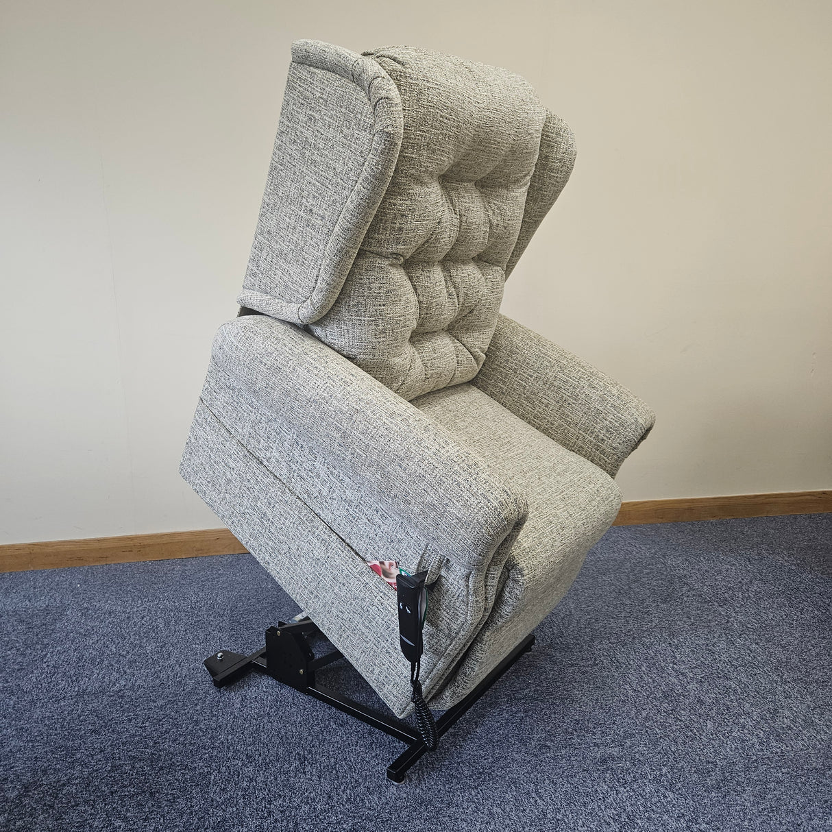 Gray upholstered chair against a white wall with a blue carpeted floor.