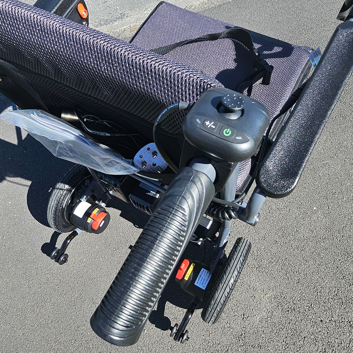 Close-up of a power chair's handlebar and control panel on a gray pavement.