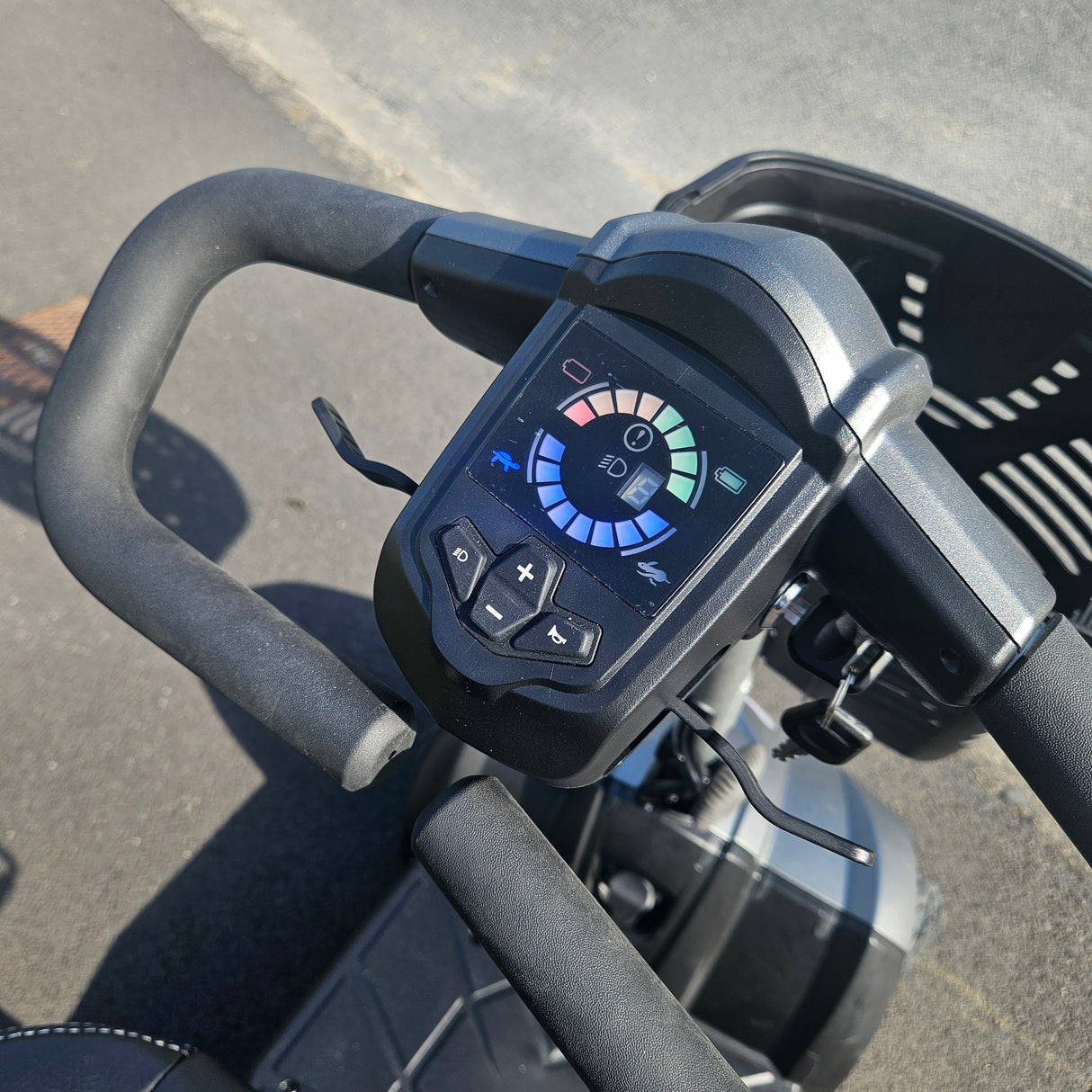 Close-up of a mobility scooter handlebar with control panel on a road