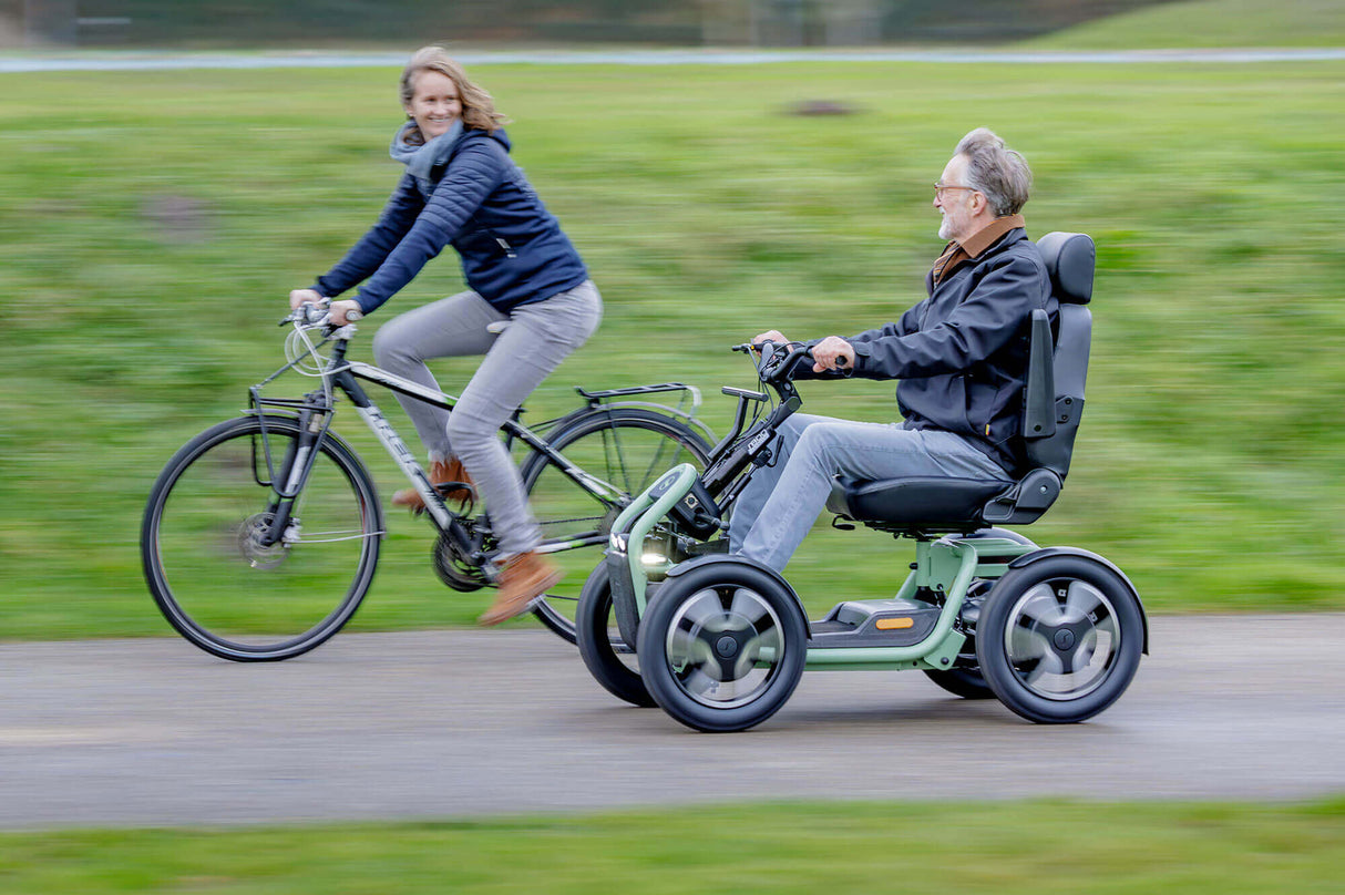 Two people, one on a bicycle and the other in a mobility scooter, riding together on a path.