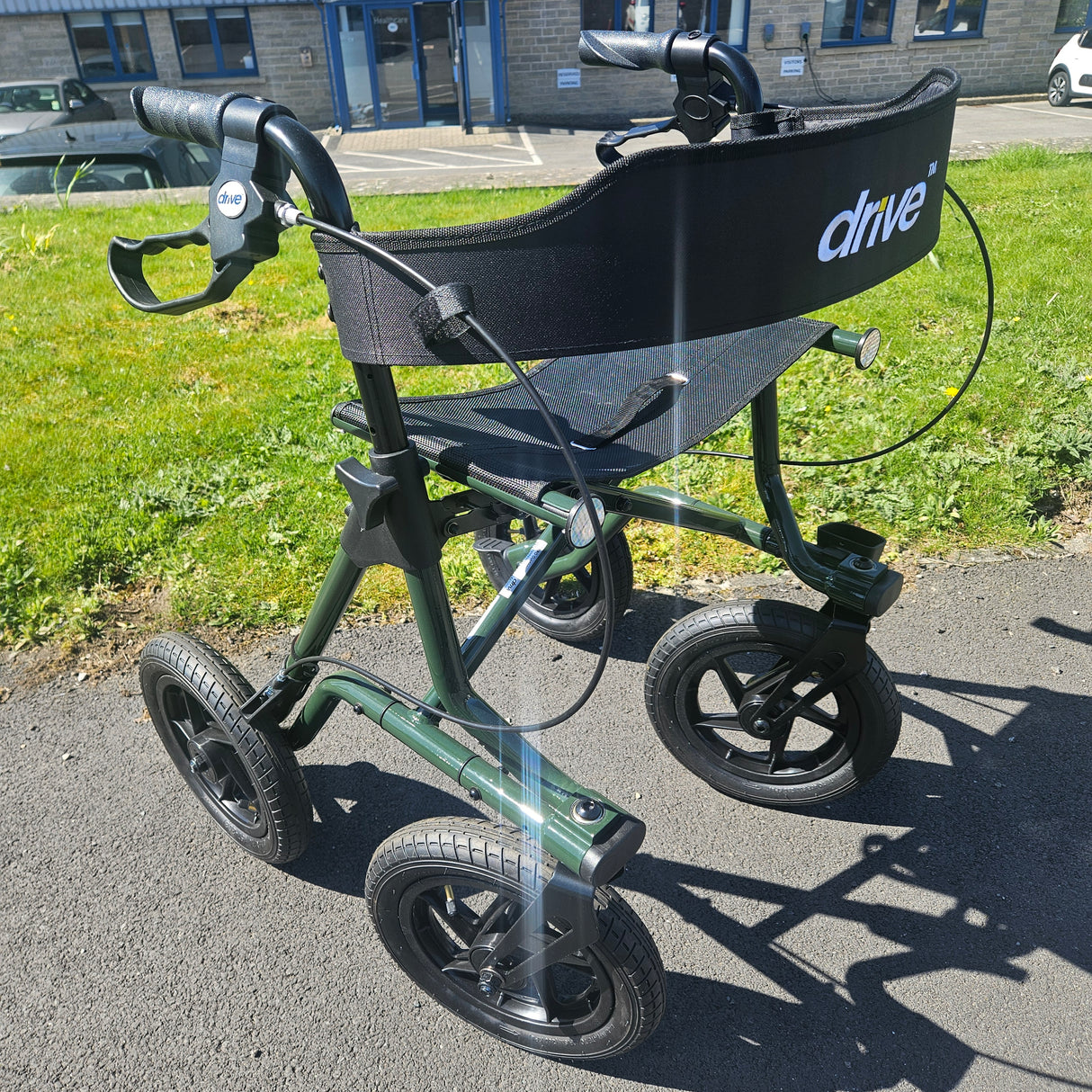 Black and green rollator on a paved path with grass