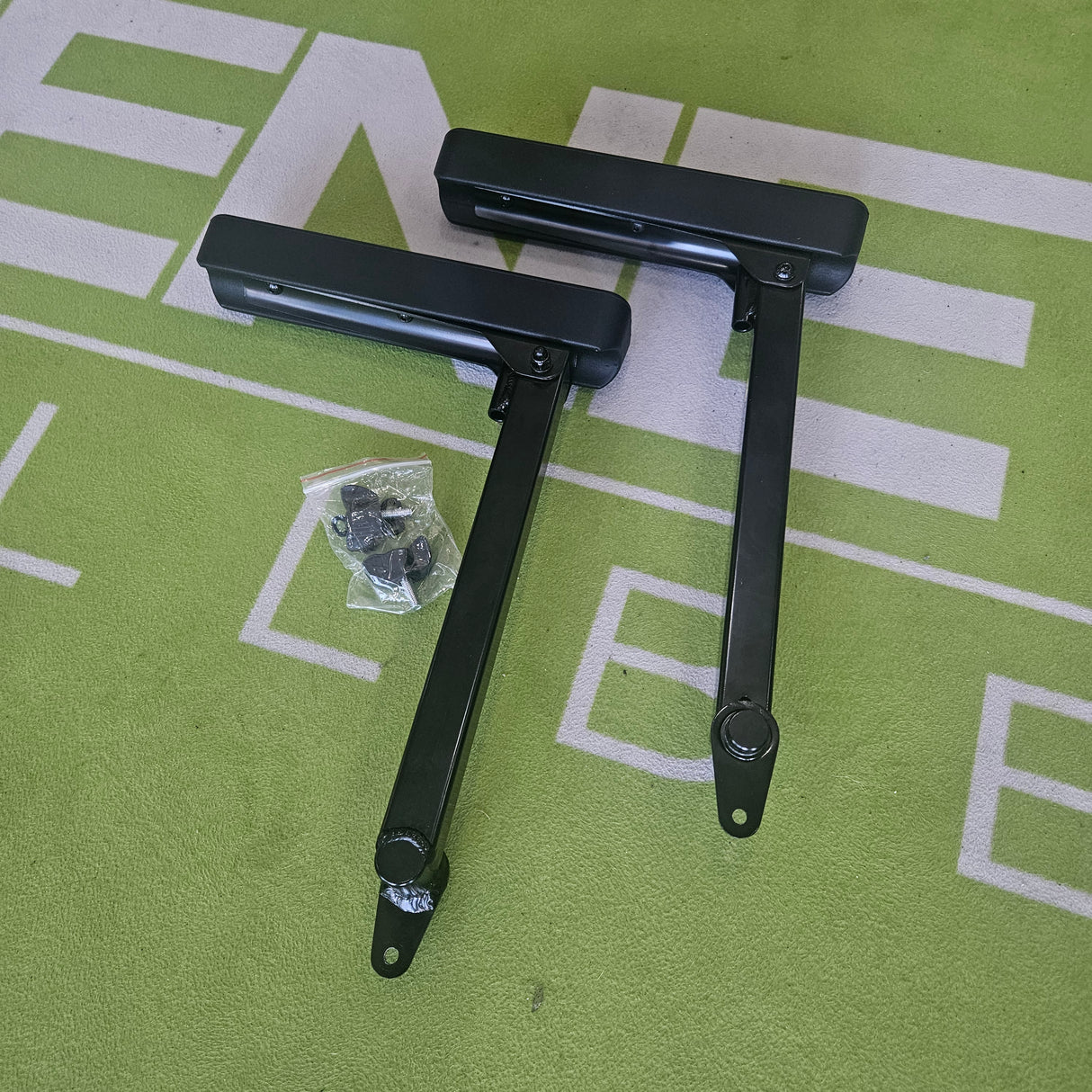 Two black metal hinges on a green surface with white text.