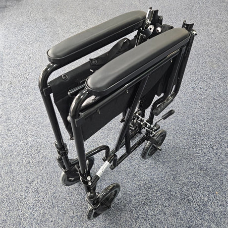 Folded black lightweight folding wheelchair with padded armrests and small rear wheels, positioned on a blue carpeted floor.