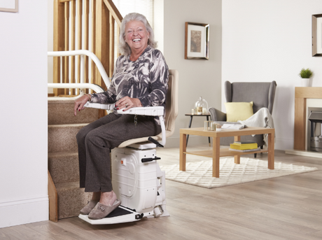 Smiling woman using a stairlift to travel safely upstairs at home, demonstrating how a stairlift supports independent living, comfort and everyday mobility.