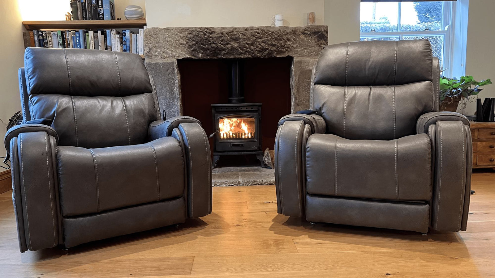 Pair of brown leather riser reclier chairs in front of log burner