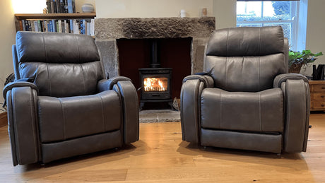 Pair of brown leather riser reclier chairs in front of log burner