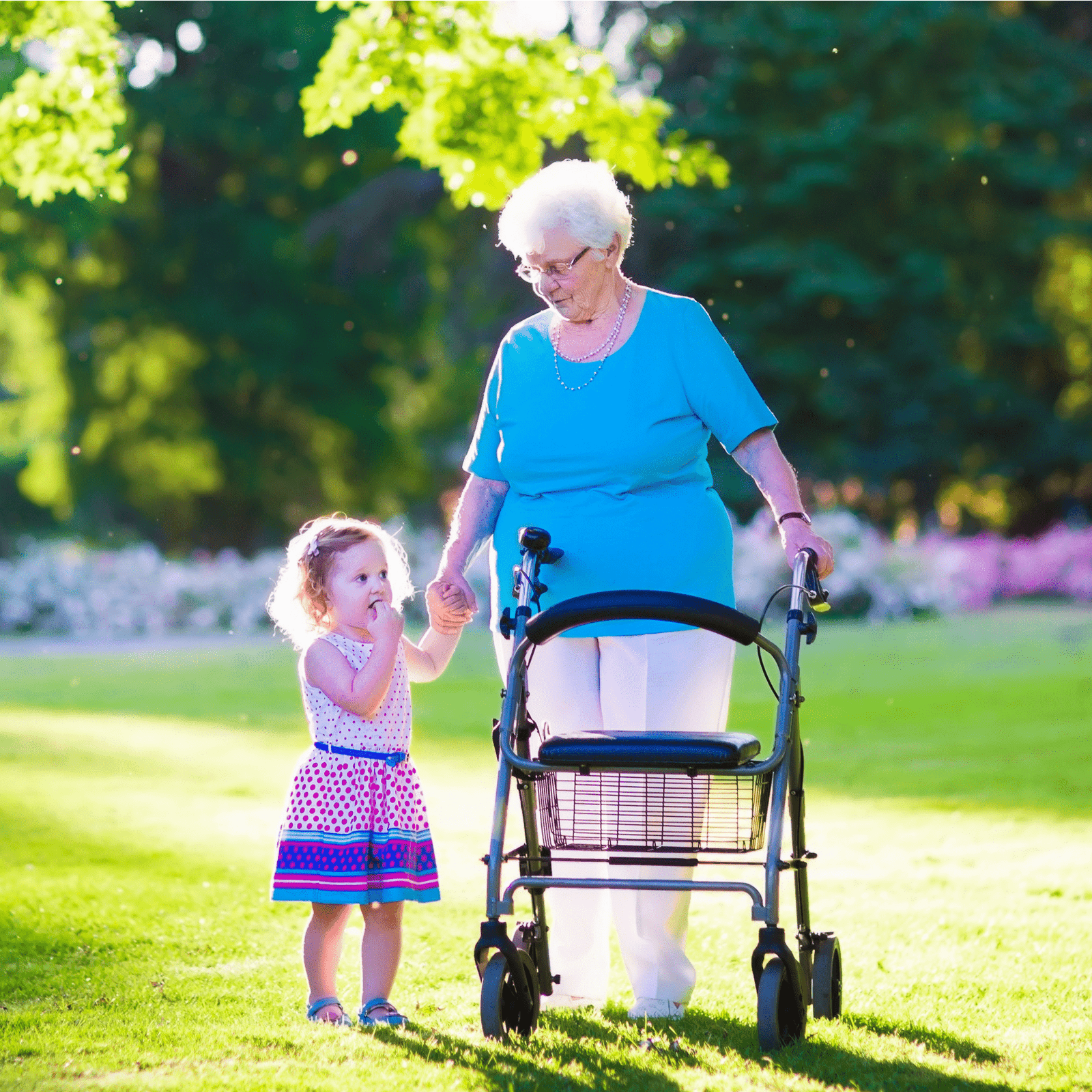 Elderly woman using a rollator while holding hands with her young granddaughter in a sunny park.