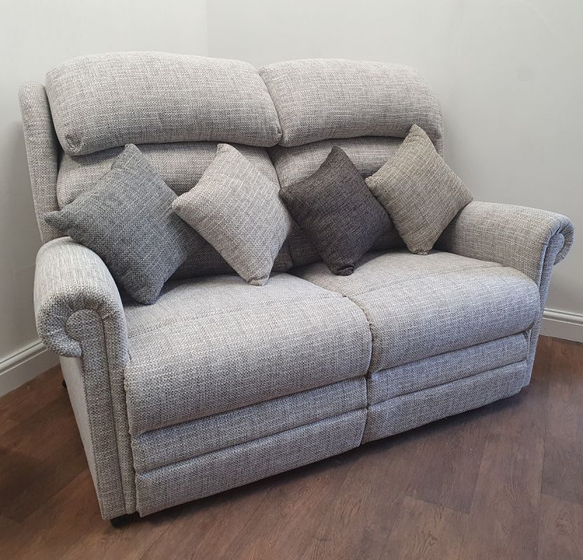 Light grey two-seater riser recliner sofa with textured fabric upholstery and five assorted grey scatter cushions, positioned on a dark wood floor against a neutral wall.