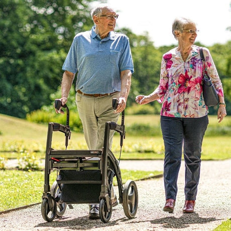 Older couple enjoying a countryside walk with a folding rollator, showcasing comfortable and portable mobility support for active travel