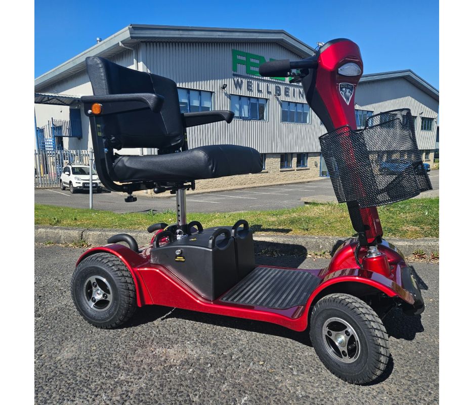 Red mobility scooter with a black seat in front of a building with 'Fenetic Wellbeing' on the sign.