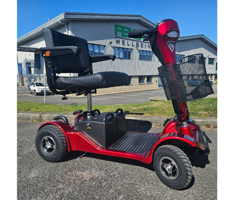 Red mobility scooter with a black seat in front of a building with 'Fenetic Wellbeing' on the sign.