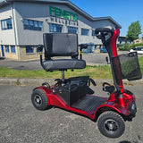 Red mobility scooter parked in front of a building with 'Fenetic Wellbeing' signage.