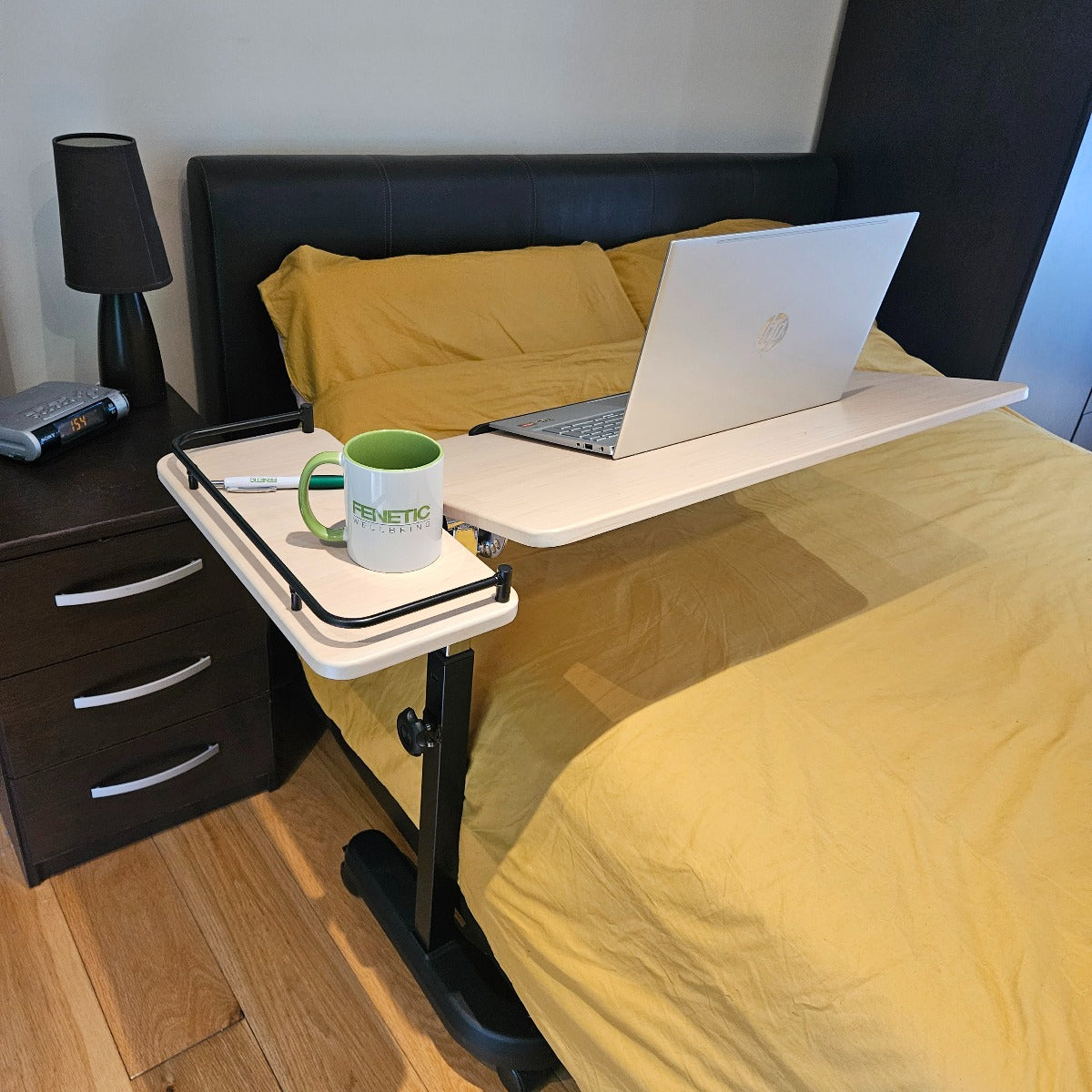 Laptop on a raised desk attached to a bed with a mug nearby.