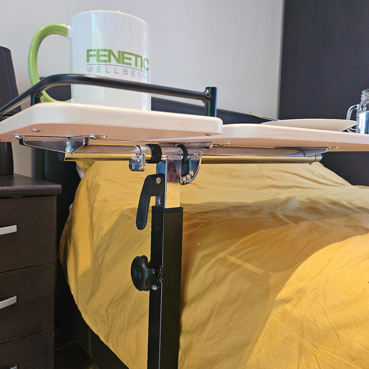 Bed with a yellow blanket and a mug on a mobility table in a room.