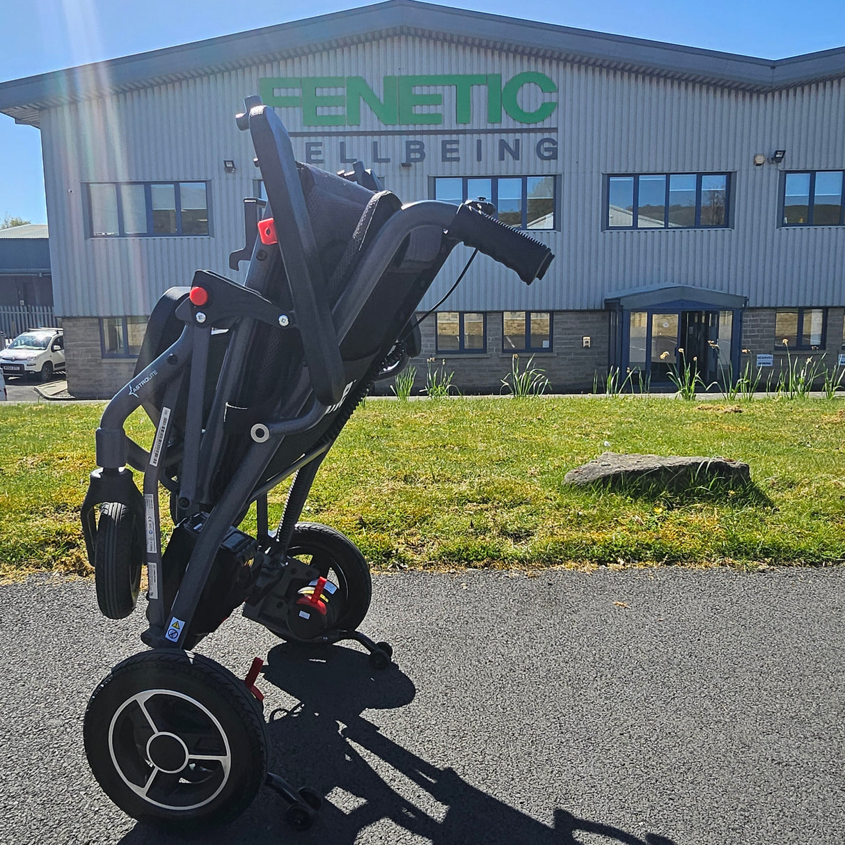 Folded powerchair on a driveway with a building in the background