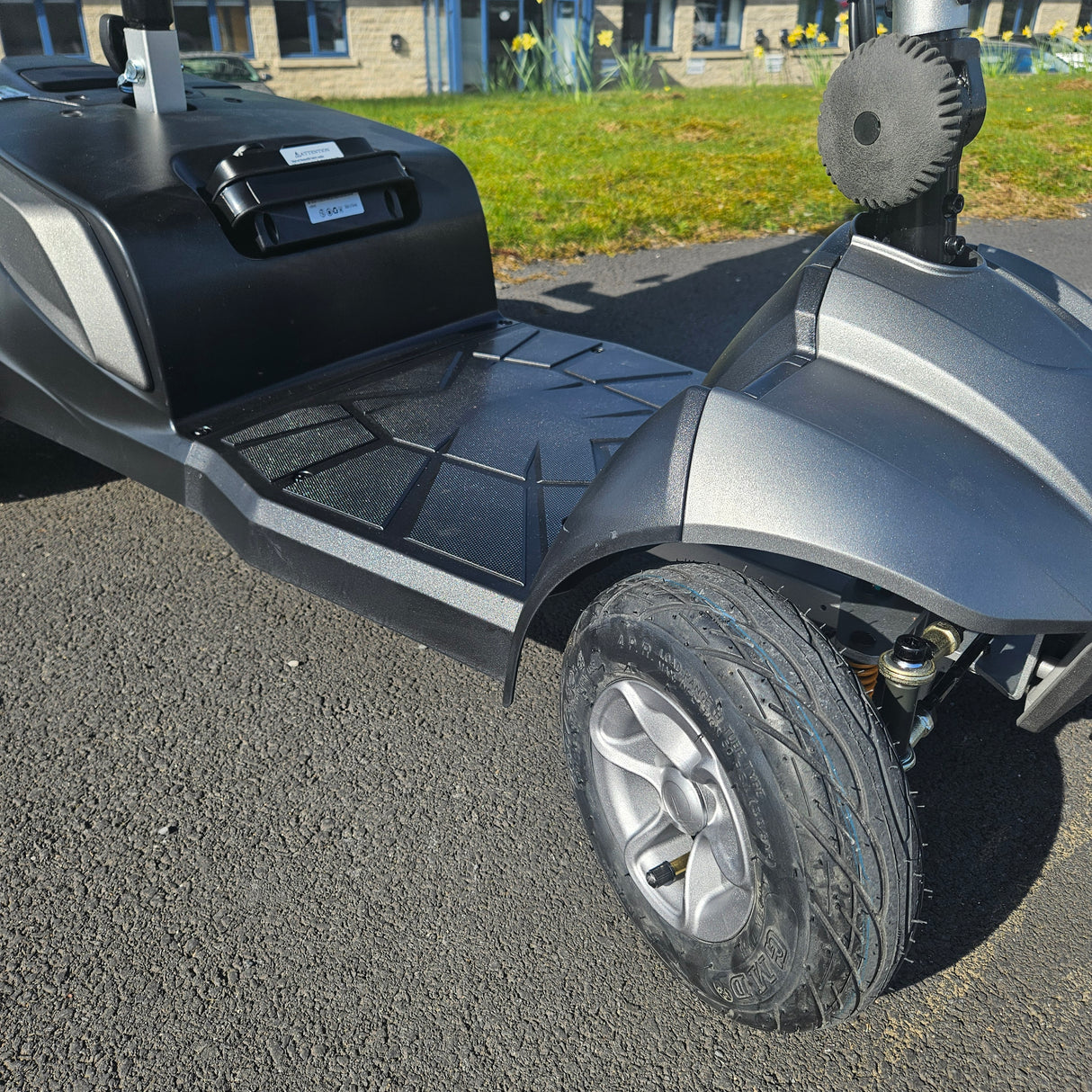 Close-up of a scooter's wheel and front section on an outdoor surface.