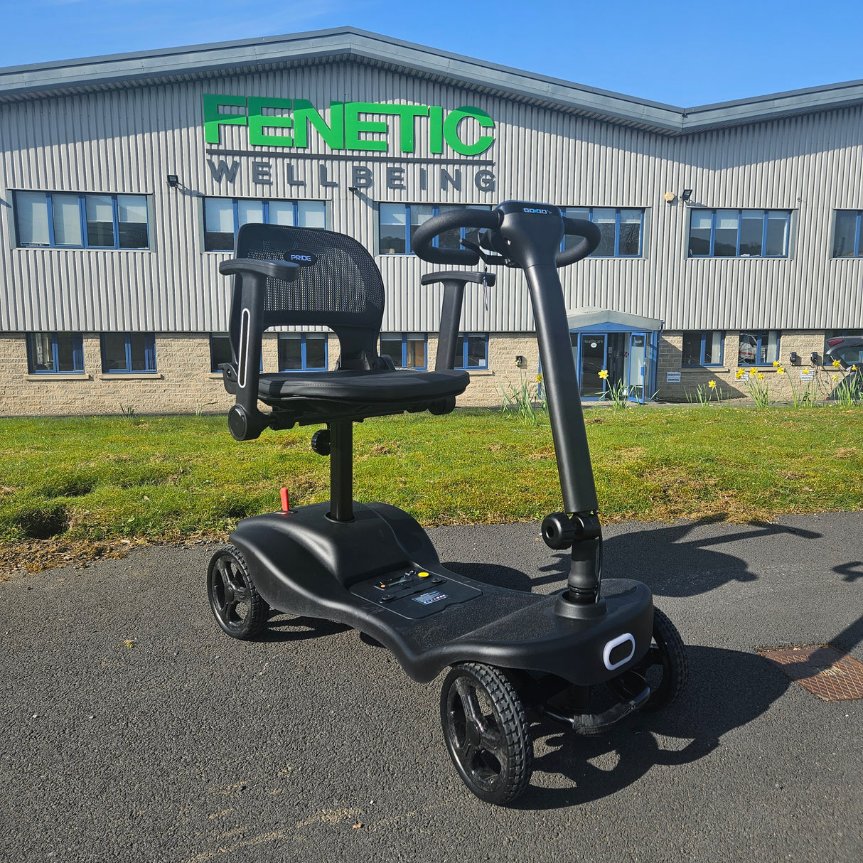 Black mobility scooter in front of a building with 'Fenetic Wellbeing' branding.