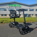 Black mobility scooter in front of a building with 'Fenetic Wellbeing' branding.