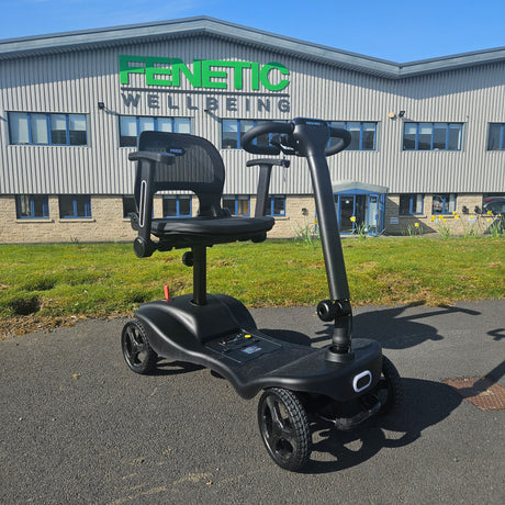 Black mobility scooter in front of a building with 'Fenetic Wellbeing' branding.