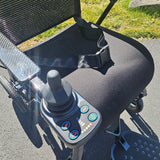 Close-up of a control panel on a powerchair with grass and pavement in the background.