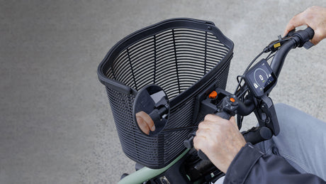 Person using a scooter with a basket attached on a gray background