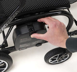 Hand reaching to open a battery compartment on a powerchair