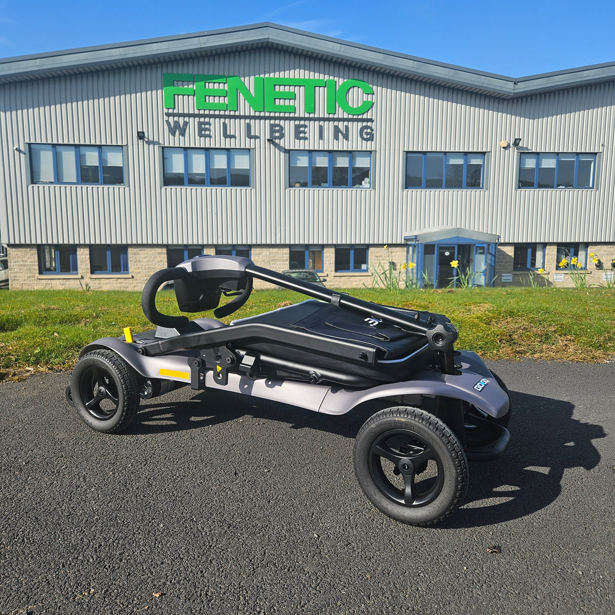 Folded mobility scooter on a paved surface with a building in the background
