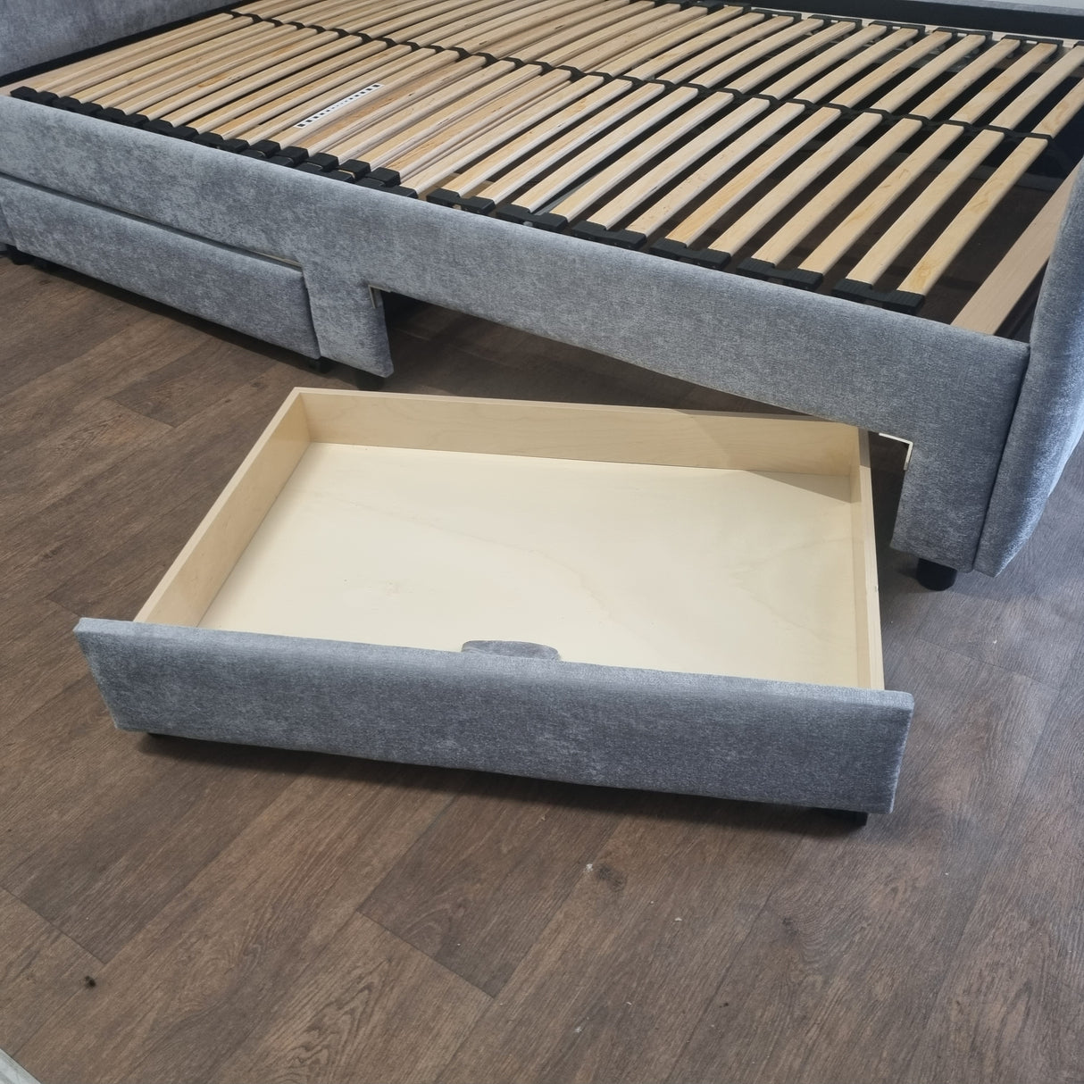 Gray upholstered bed with an open drawer on a wooden floor