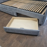 Gray upholstered bed with an open drawer on a wooden floor