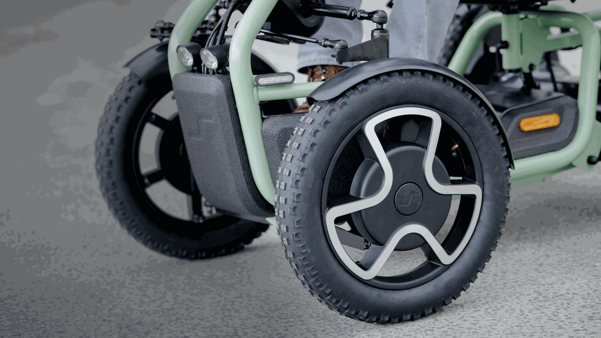 Close-up of a green mobility scooter with large wheels on a gray surface