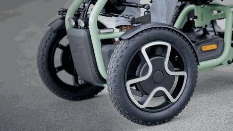 Close-up of a green mobility scooter with large wheels on a gray surface